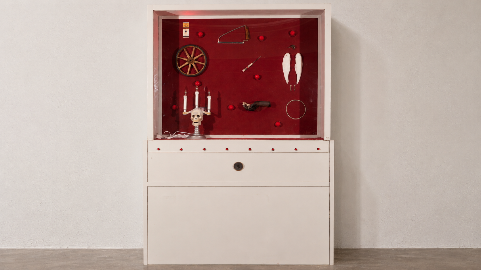White museum cabinet containing eight objects in a burgundy felt-lined case, with eight red buttons below the glass.